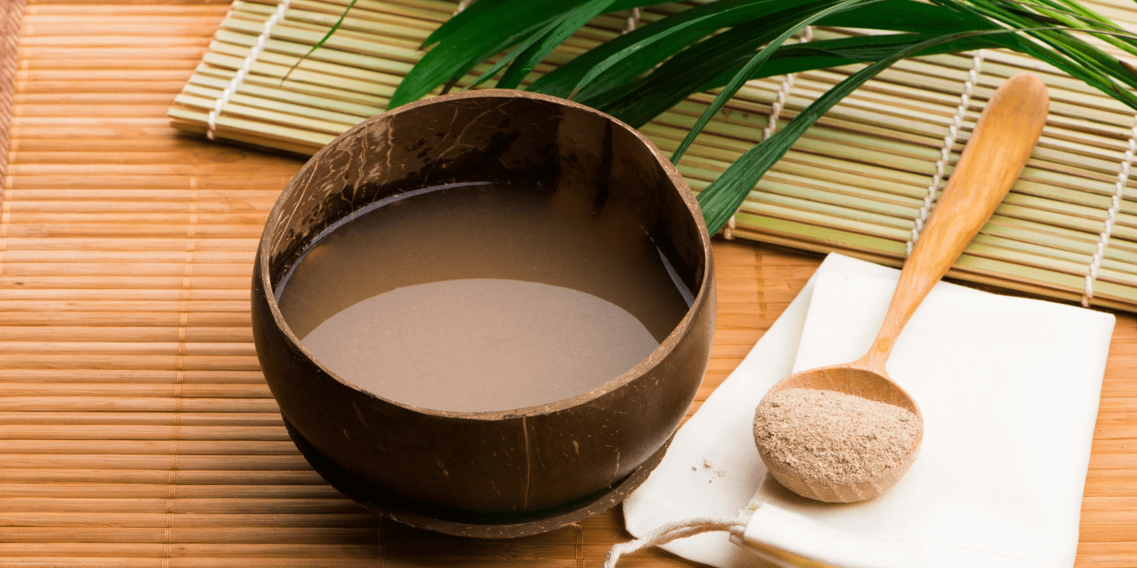 Traditional kava drink in a wooden bowl on a bamboo mat with kava root and strainer